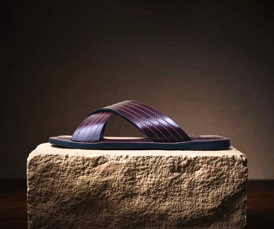 An oxblood leather sandal, hand-stitched, resting on stone